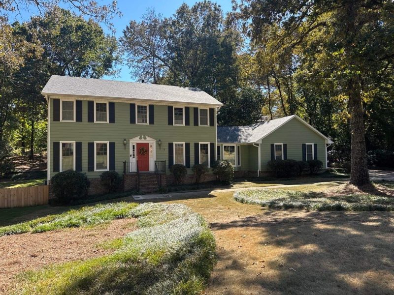 Completed residential roofing project on a green two-story home surrounded by trees
