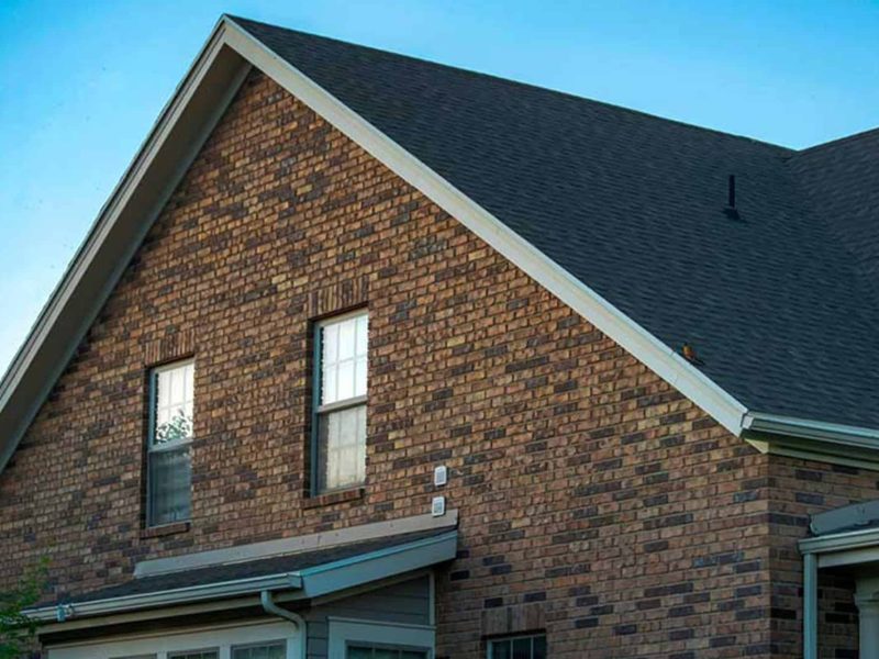 Residential brick home with a newly installed dark shingle roof and finished roofline